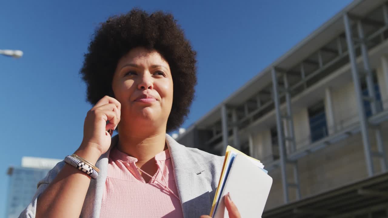 más tamaño mujer biracial hablando en el teléfono inteligente y sosteniendo cuadernos en la ciudad