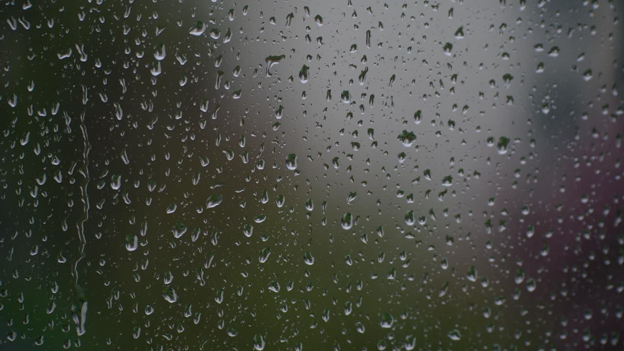 Raindrops on home window with few moving down, blurred background