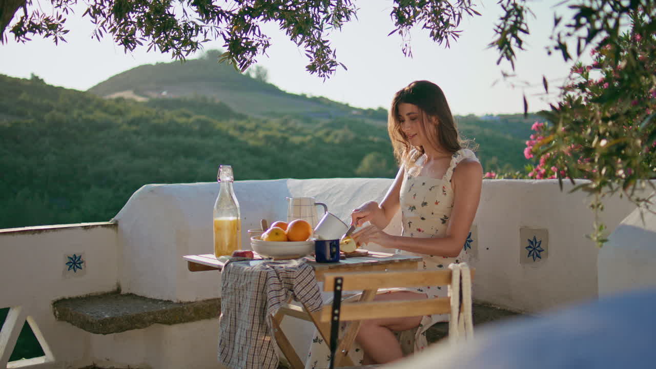 테라스에서 아침 식사를 준비하는 과일을 들고 있는 조용한 모델. 사과를 잘라내는 여자