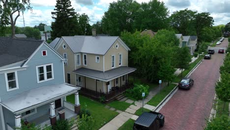 Aerial-shot-of-a-quaint,-tree-lined-residential-street-with-brick-road,-showcasing-traditional-American-homes-and-parked-vehicles