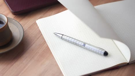 open notebook with pen and coffee cup on a wooden table