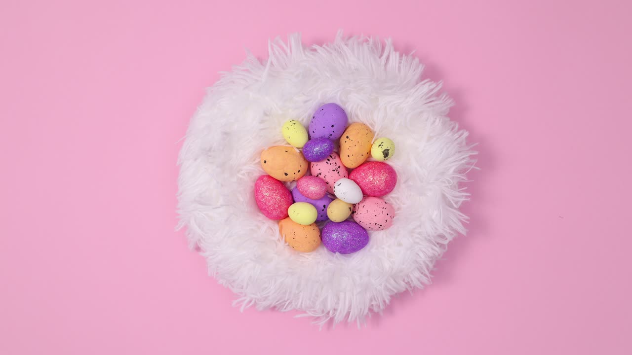 Easter eggs appear in fur nest on pastel pink background. Stop motion flat lay