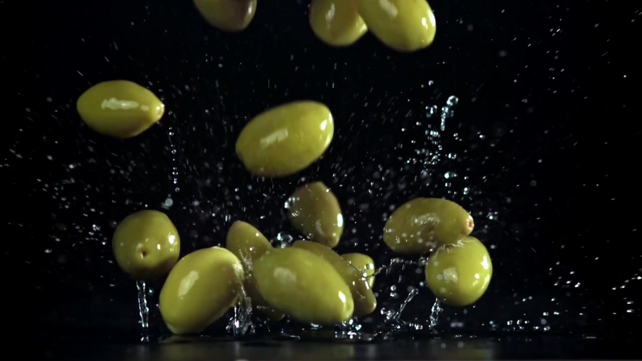 Movimento rallentato di olive verdi che cadono e schizzano su superficie nera