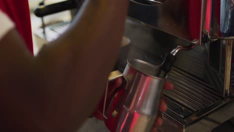 sección media de un barista afroamericano usando una máquina de café espumando leche en una cafetería