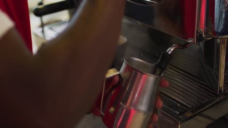 midsection of african american barista using coffee machine frothing milk in cafe