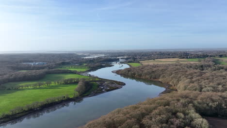 Aerial-flying-over-Hamble-River-with-winter-trees,-boat-harbour-and-bridges-in-the-distance-UK-4K