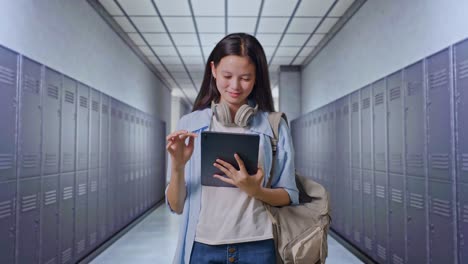 estudiante adolescente asiática con una mochila usando una tableta y apuntando a un lado mientras está de pie en el pasillo