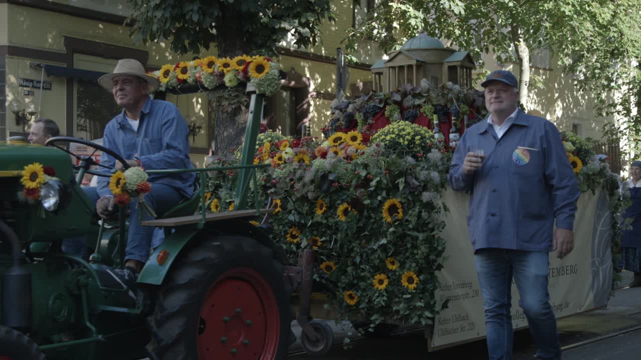 Pan shot of a Wine producer drives a tractor adorned with vibrant sunflowers, at the Cannstatter Volksfest Historical Parade, in Stuttgart Bad Cannstatt, Baden-Württemberg, in Germany
