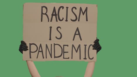 an unknown person is holding a poster from a cardboard box with the words racism is a pandemic with both hands. equality and unity concept. isolated a green screen, chroma key. close up. slow motion