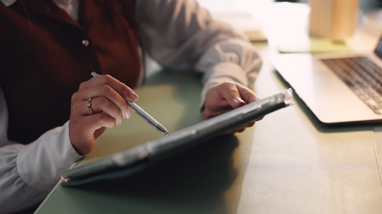 Woman using tablet and stylus at desk with laptop