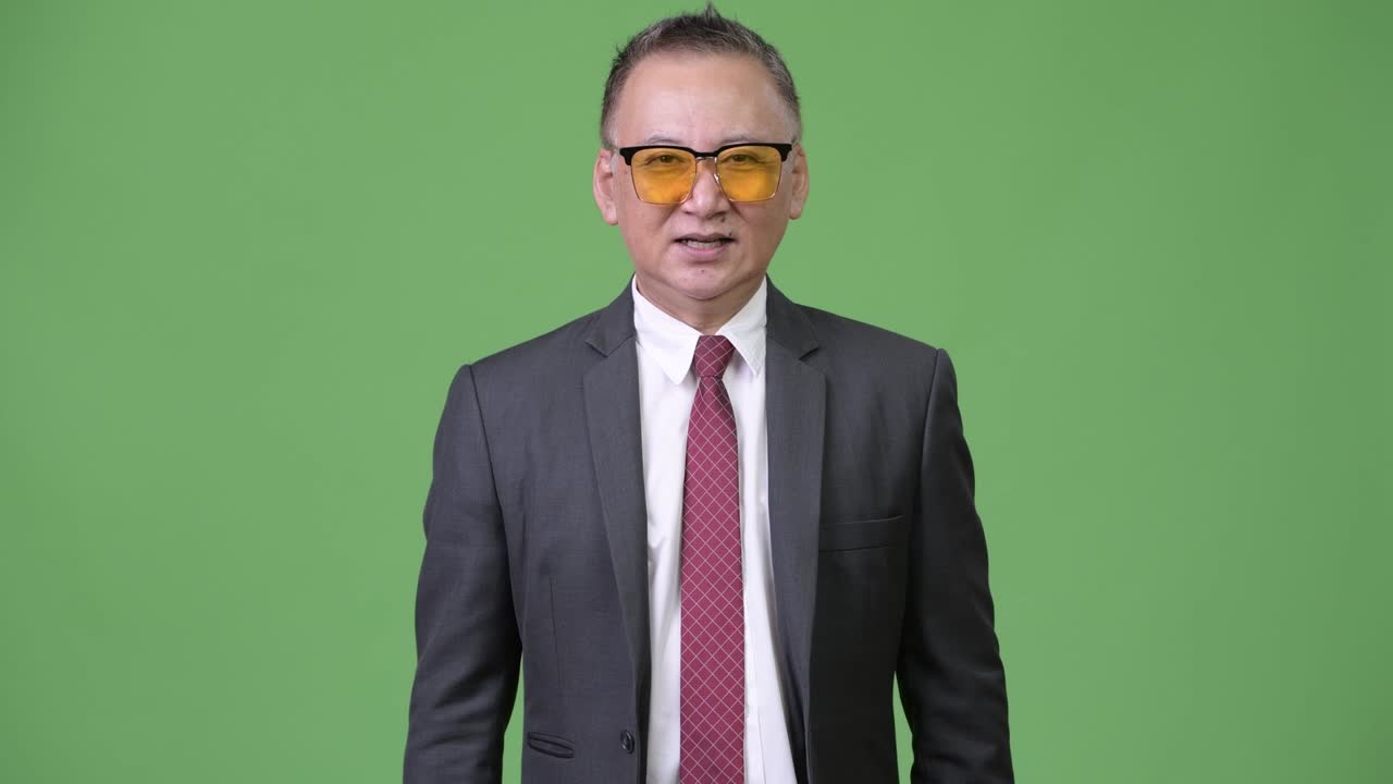 Uomo d'affari giapponese maturo che indossa occhiali da sole su sfondo verde