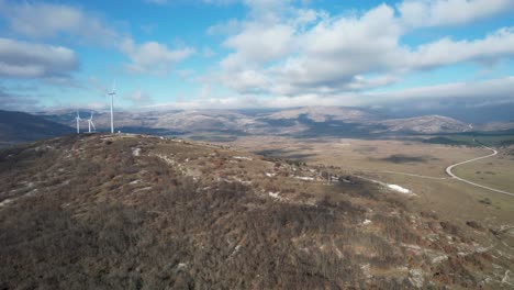 Beautiful-aerial-shot-of-Croatian-landscape-with-wind-turbines-generating-renewable-energy-in-the-background-and-an-empty-road,-in-the-region-of-Lika-in-Croatia,-Europe