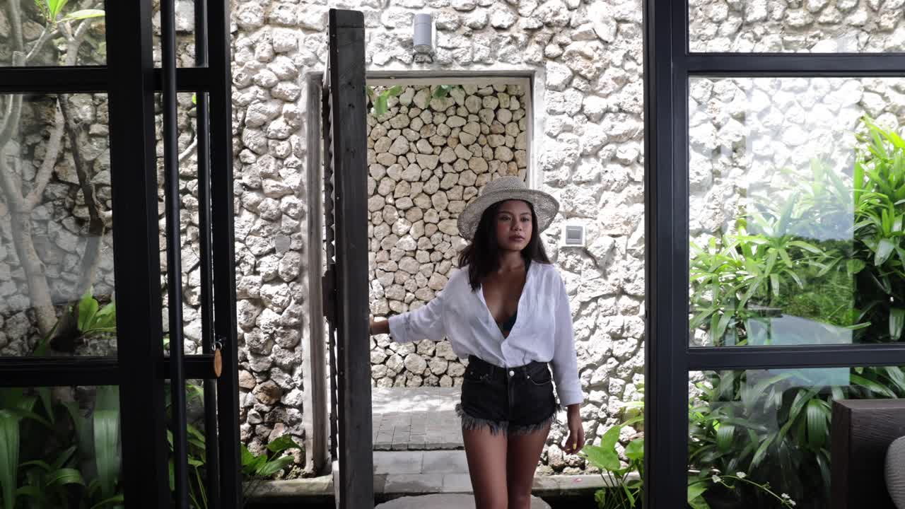 joven modelo asiática entrando a una gran sala de estar en una villa tropical de lujo en bali, indonesia, en un día soleado