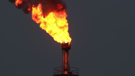 Oil-gas-refinery-flare-set-ablaze-releasing-large-red-black-plume-into-night-sky