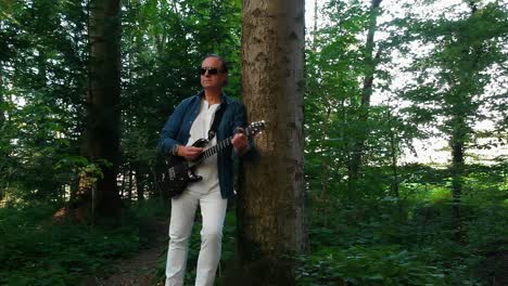 a male professional musician playing guitar in the woods