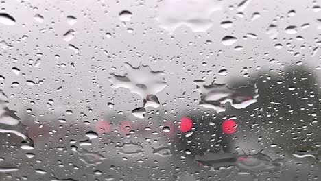 Close-up-of-rainy-depressive-weather-over-windscreen-and-red-blurred-lights-of-car-traffic-in-background-with-wiper-cleaning-windshield-from-raindrops