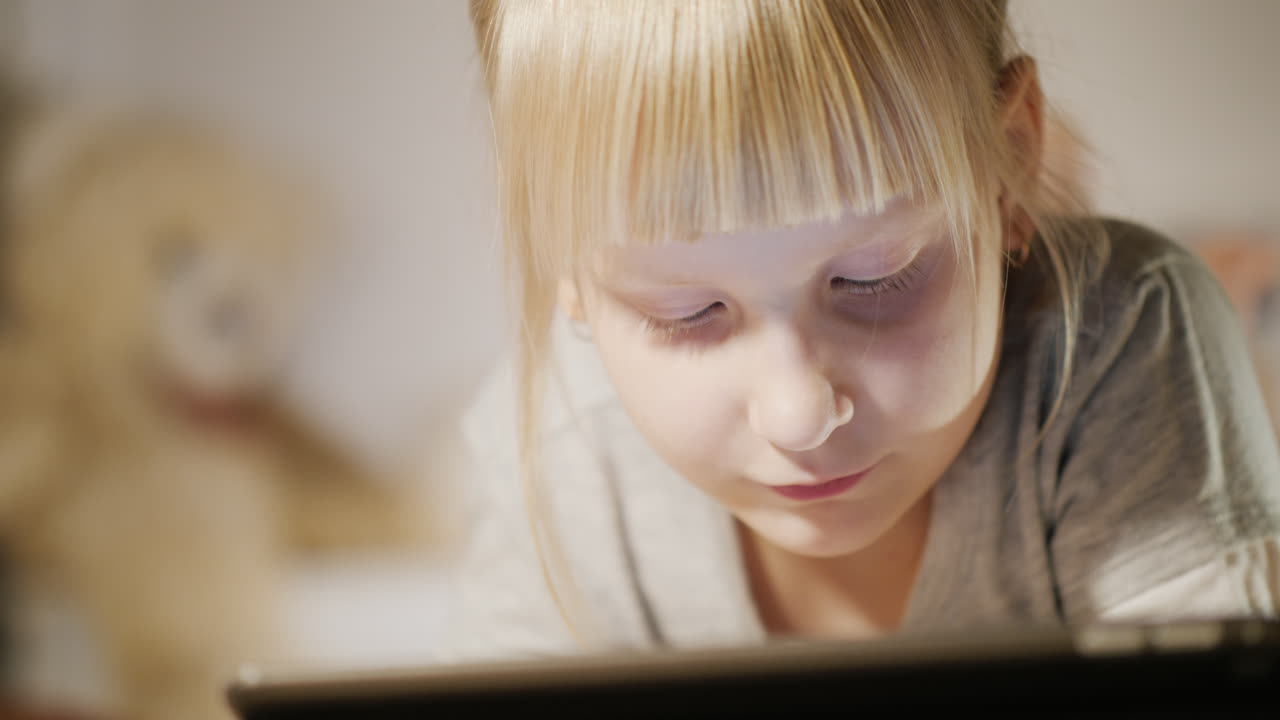 침실이 있는 태블릿을 즐기는 아이의 초상화는 저녁에 침대에 누워 있다