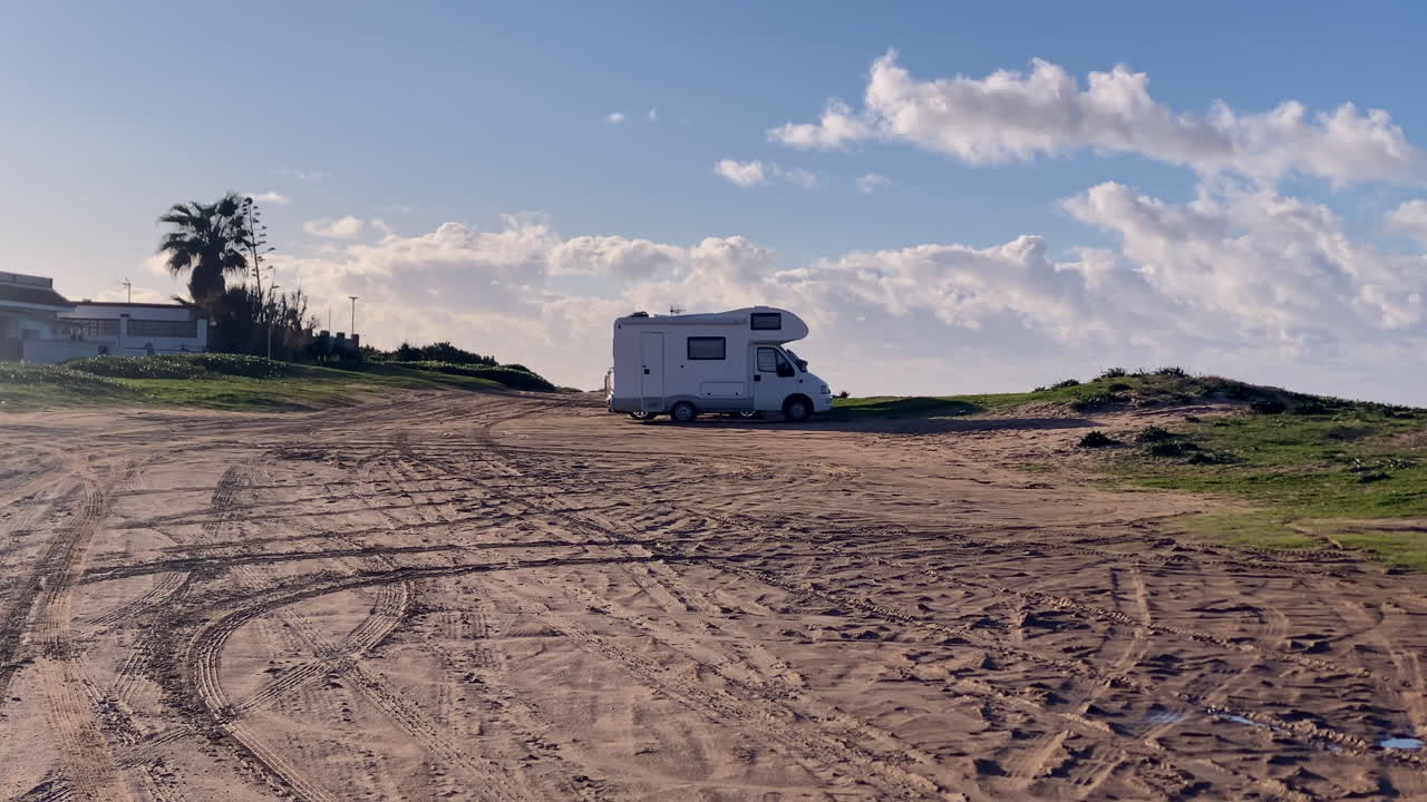 Furgoneta camper aparcada en un terreno costero arenoso cerca de la playa bajo un cielo abierto