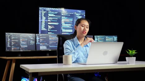 asian female programmer thinking about something while writing code by a laptop using multiple monitors showing database on terminal window desktops in the office