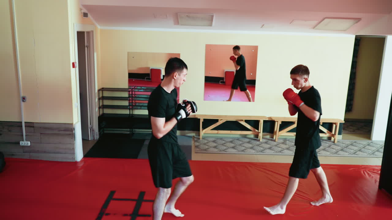 Karate practitioners performing sparring drills on red mat inside martial arts gym, demonstrating fighting stance, focus, power, with gloves during intense training session in controlled environment