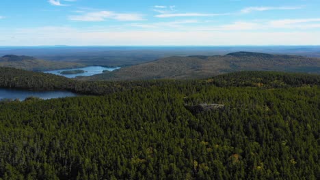disparo aéreo de un dron deslizándose sobre un gran bosque verde con lagos y un afloramiento rocoso en el desierto de maine
