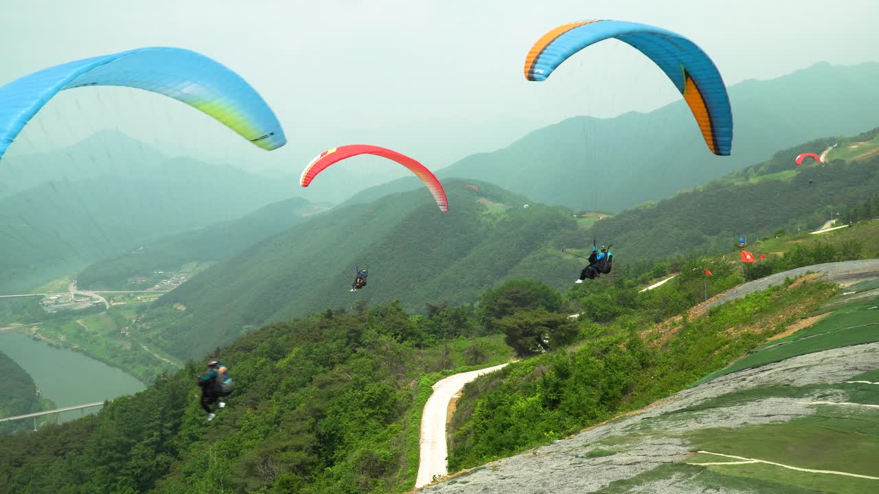한 무리의 사람들이 한국 단양 산에서 동시에 탠덤 패러글라이딩을 타고 있습니다.