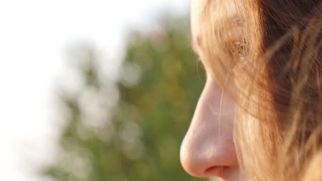 Close-up-profile-shot-of-a-beautiful-girl-staring-off-into-the-distance-as-the-bright-morning-sun-shines-on-her-face,-then-she-turns-to-look-at-the-viewer