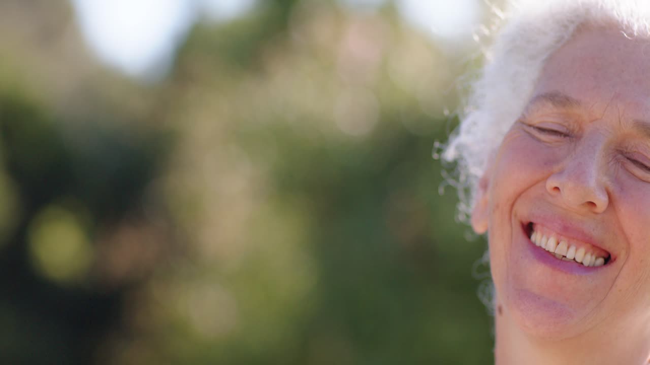 La telecamera si allontana rivelando una donna afroamericana anziana che inclina la testa e sorride in un parco, con spazio per il testo.