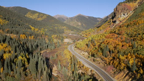 Aerial-shot-forward-of-vast-and-wide-Colorado-mountain-roads-and-bright-yellow-and-orange-aspen-trees-during-autumn-in-the-San-Juan-Mountains-along-the-Million-Dollar-Highway-road-trip