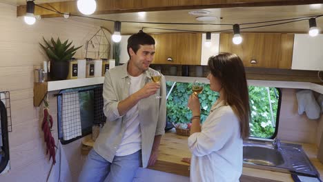 pareja feliz sosteniendo copas con vino blanco disfrutando hablando en una pequeña cocina en la furgoneta. familia marido y mujer bebiendo, celebrando aniversario romántico juntos en las ruedas de la casa de vacaciones