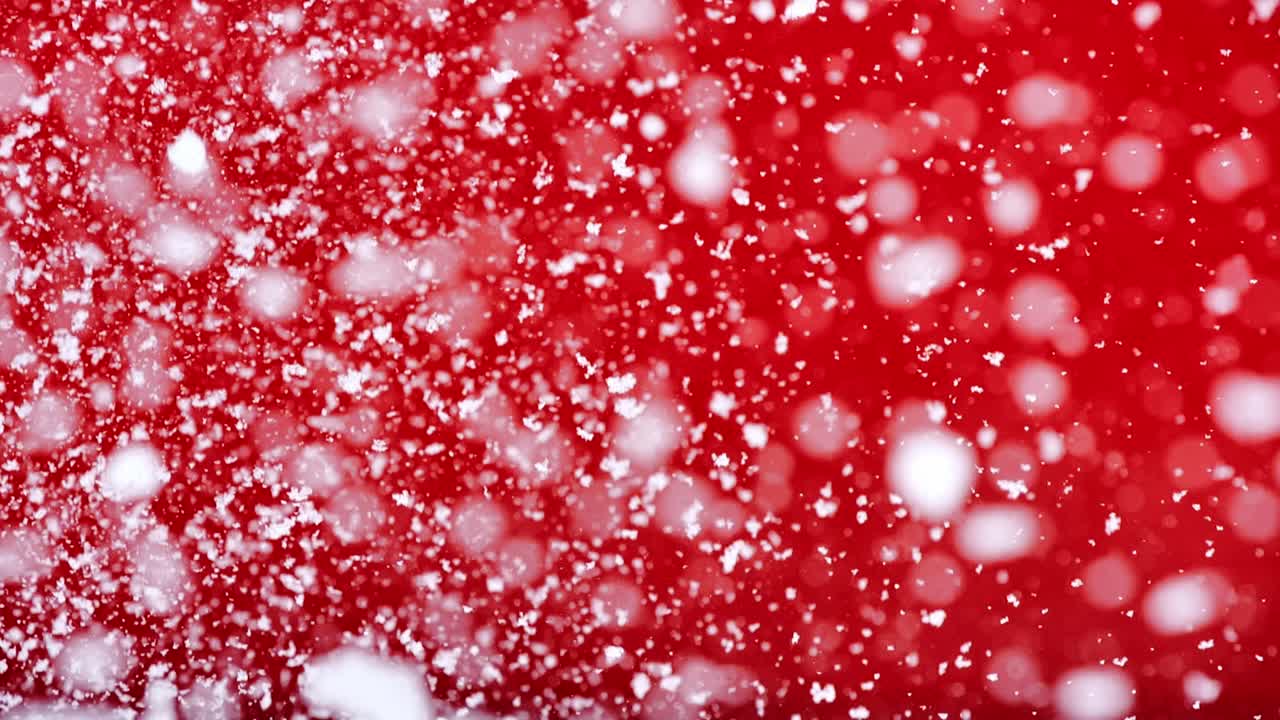 Magical snowfall, white flakes descending against vivid red backdrop slow motion