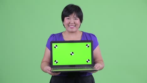 초록색 배경에 미소 짓는 동안 컴퓨터에서 크로마 키를 보여주는 짧은 헤어 스타일의 과체중 아시아 여성의 초상화