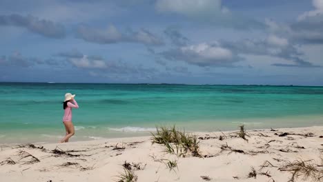 young woman talks on phone while walking alone on white sand beach, caribbean sea