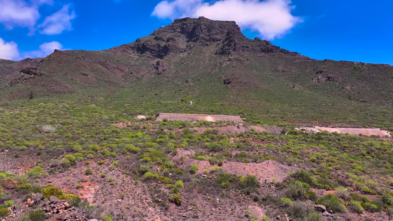 Volcanic Adeje mountain and old Acequia under blue sky, green bushy Tenerife landscape