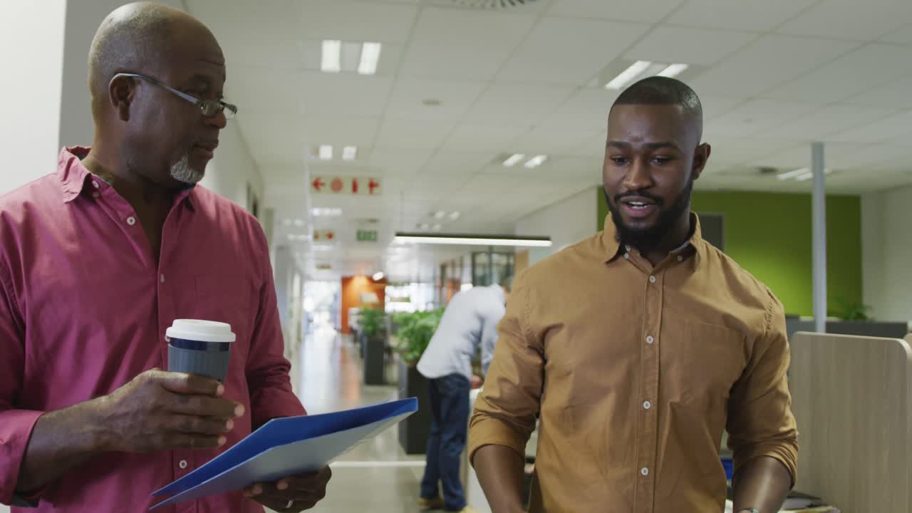 Happy african american male business colleagues talking and walking in office