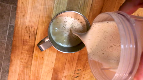 se vierte café cetogénico a prueba de balas con mantequilla de una licuadora a una taza de acero inoxidable