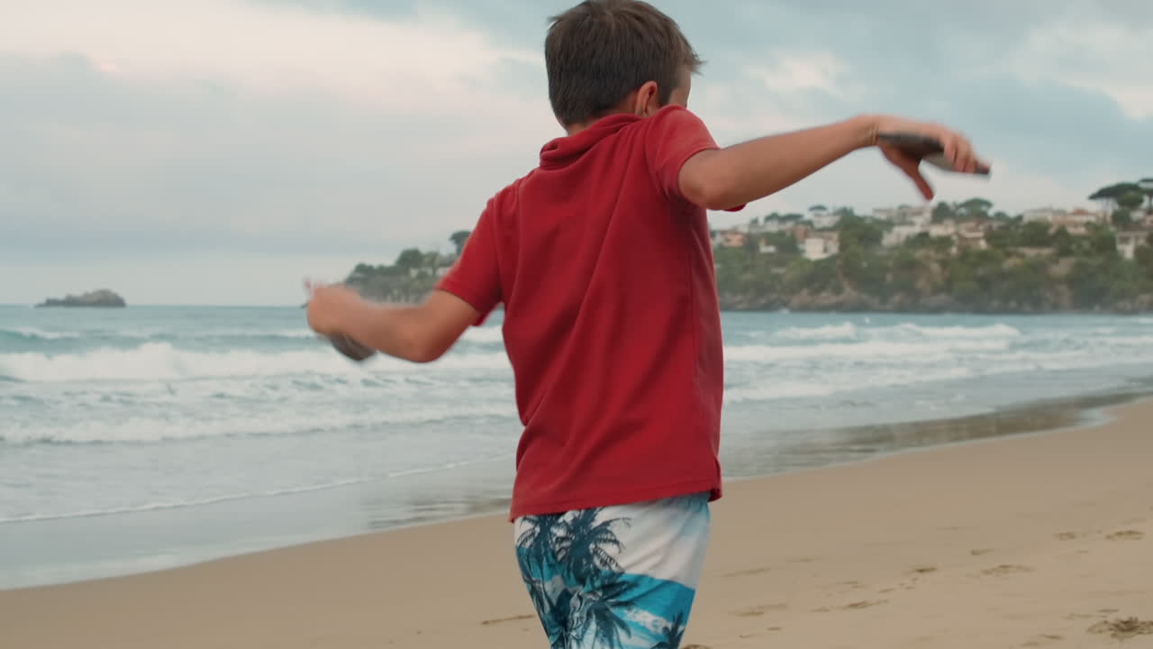 Chico activo bailando en la orilla del mar. Joven despreocupado disfrutando el verano en la playa de arena.