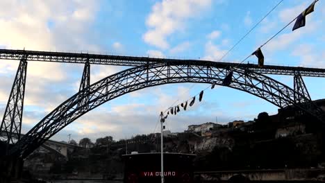Rabelo-Boot-Mit-Flaggen,-Das-Auf-Dem-Fluss-Douro-In-Porto-Fährt-Und-Die-Brücke-Von-Dona-Maria-Pia-überquert