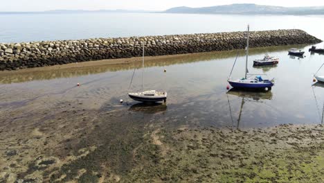 Aerial-view-boats-in-shimmering-low-tide-sunny-warm-Rhos-on-Sea-seaside-sand-beach-jetty-coastline-orbit-left