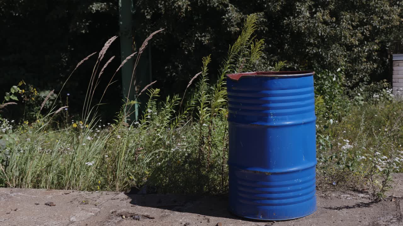 снимок вверх ржавой синей металлической бочки, брошенной на тротуаре