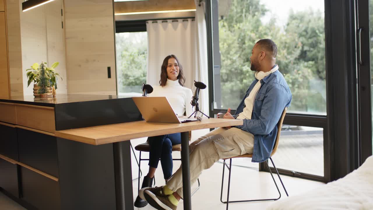 Diverse hosts starting discussion in home office studio, man speaking into mic while woman laughing