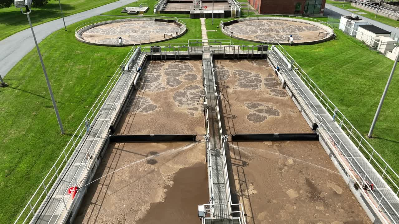 Ripresa aerea con tilt verso l'alto che mostra l'acqua sporca e ribollente delle vasche di un impianto di trattamento delle acque reflue. Giornata di sole in una città americana