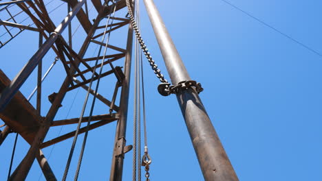 metal chain with a hook sliding down by the metal pipe. low angle view on the tower at the site for drilling oil.