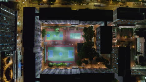 top-down drone view of illuminated public sports courts surrounded by residential towers