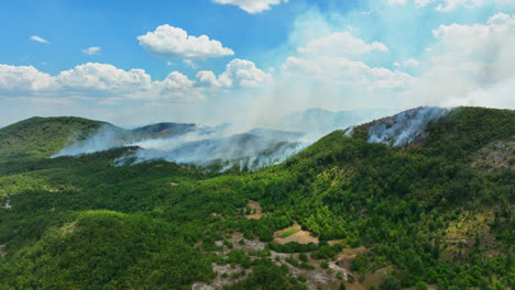 aerial: raging wildland fire in a green nature and hill landscape, summer day