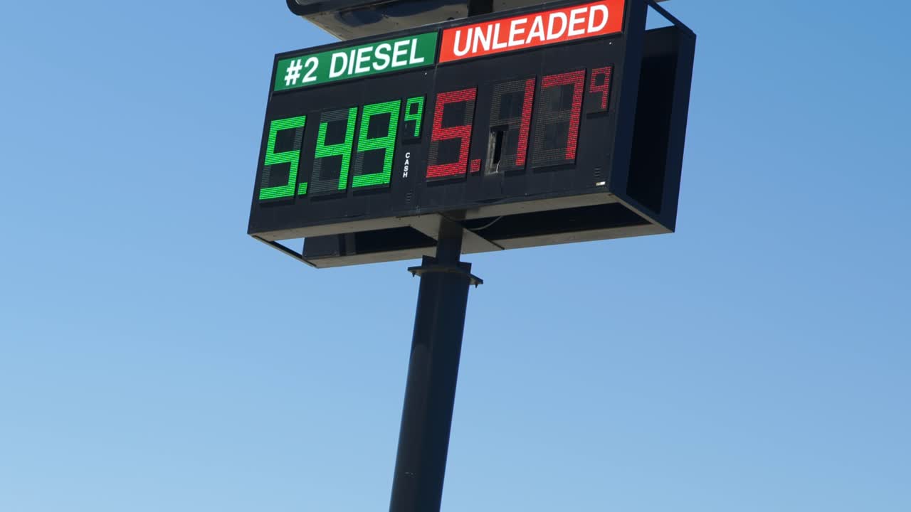 Gas Station Pump Prices High Over 5 Five Dollars Per Gallon 5.17 Unleaded 5.49 Diesel Tall Outdoor Sign Flickering on a hot heat stroke sunny blue sky summer day zooming in and panning up.