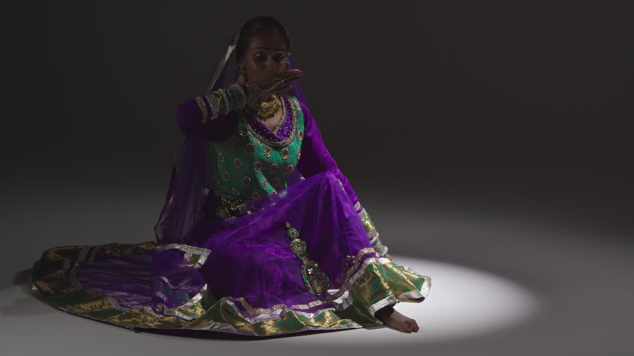 bailarina de kathak femenina realizando un baile vestida con el vestido tradicional indio sentada en el suelo en el centro de atención 2
