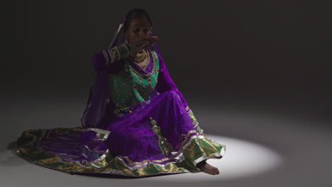 Female-Kathak-Dancer-Performing-Dance-Wearing-Traditional-Indian-Dress-Seated-On-Floor-In-Spotlight-2