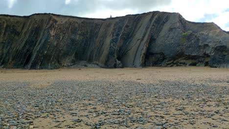 Tall-slate-rocks-aligned-vertically-forming-a-cliff-a-few-metres-high-in-Widemouth-beach-in-Conrwall,-England