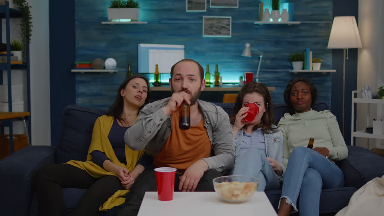 Amici multietnici che guardano un video divertente in televisione seduti sul divano.